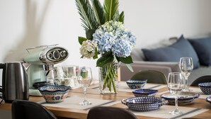 Una mesa de comedor dispuesta con cuencos de diseño azul y blanco, copas de vino transparentes, y un florero con hortensias azules y hojas verdes.