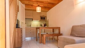 Un ambiente compatto con angolo cottura, un tavolo di legno con panche e un divano.