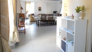 Un vaste espace de vie comprenant une table et des chaises, une bibliothèque et une grande fenêtre agrémentée de rideaux.
