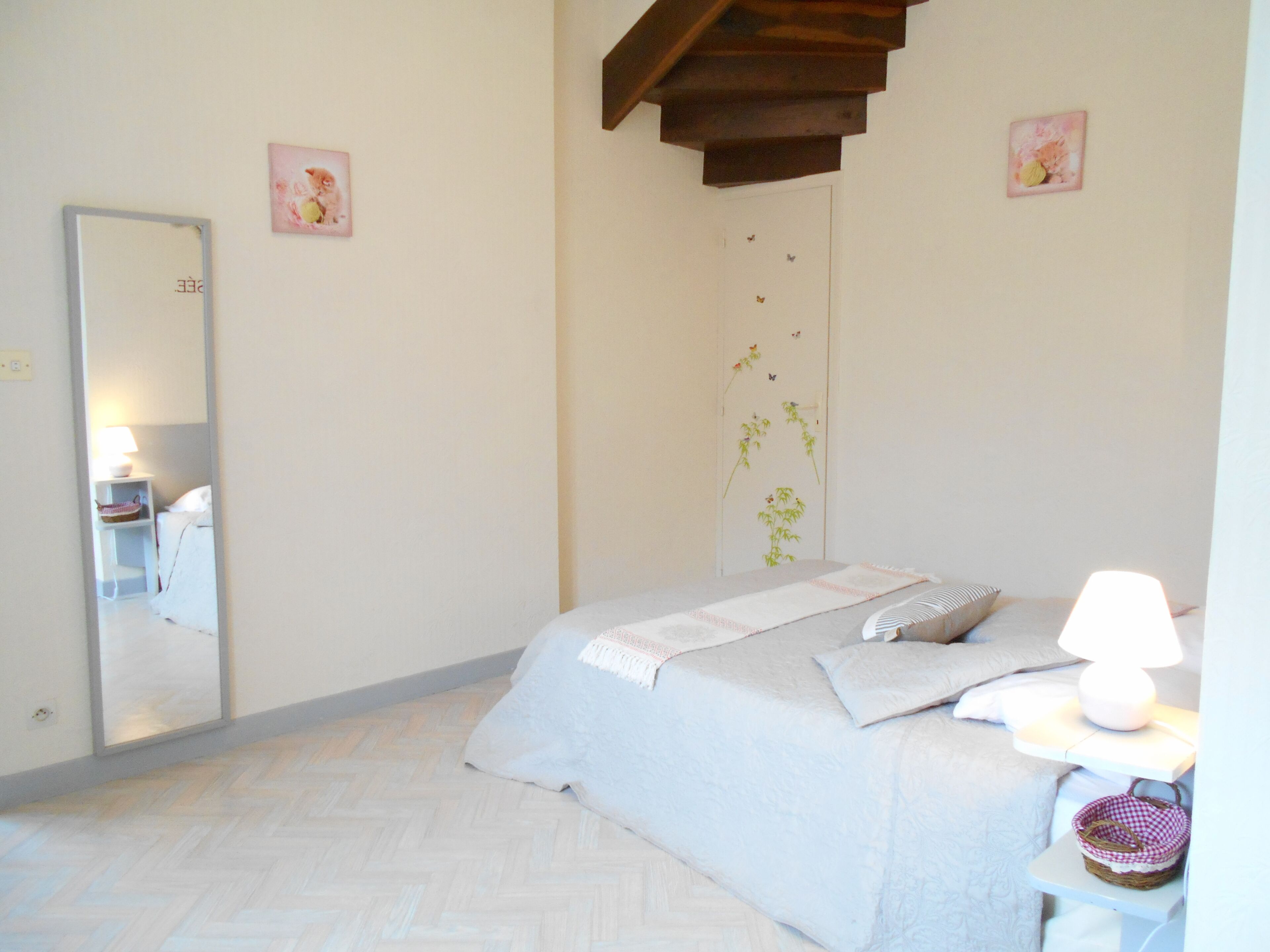 A bedroom with a bed, a bedside table with a lamp, a mirror, and a wall with a floral decoration.