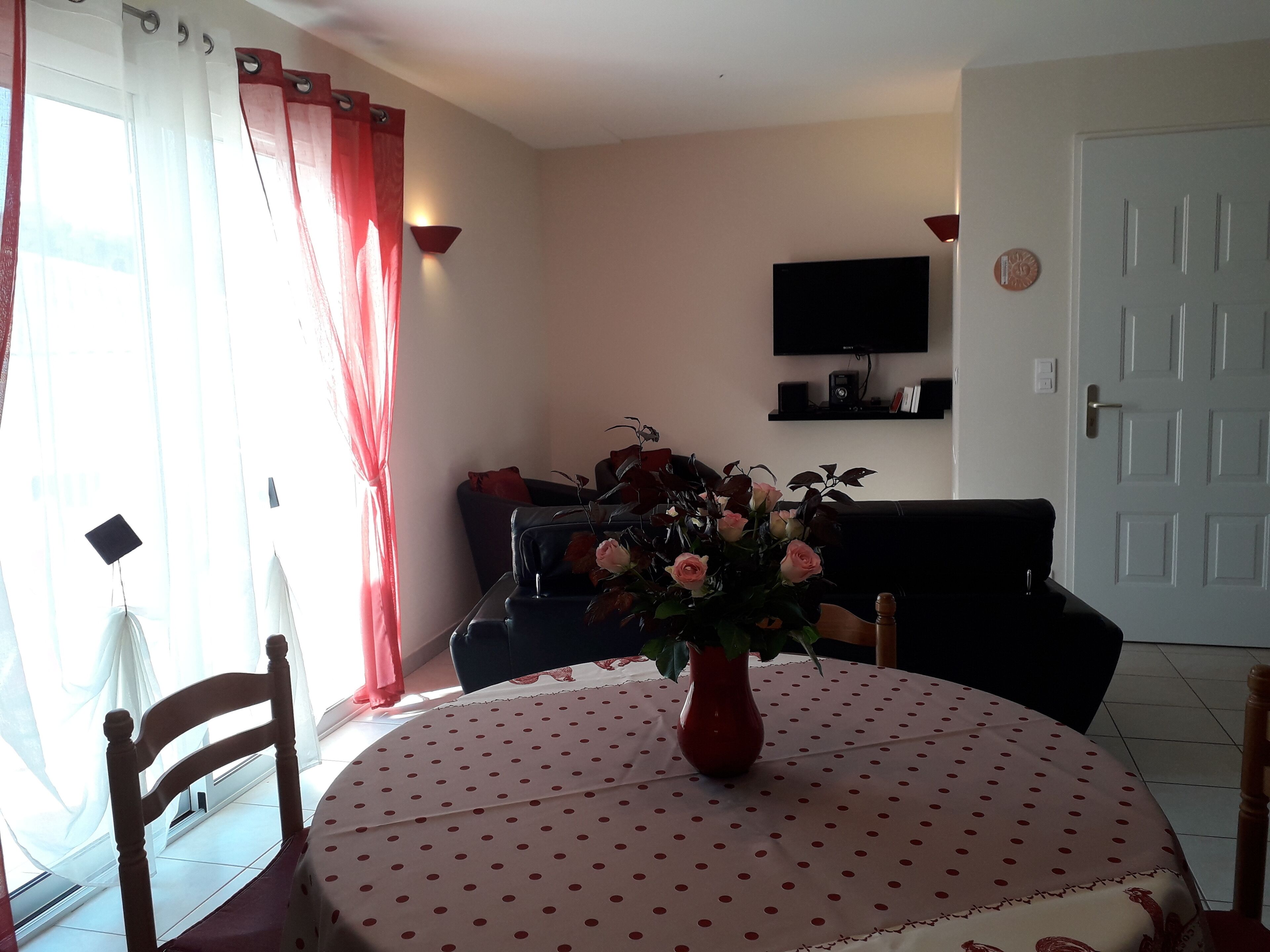 Un área de comedor con una mesa redonda cubierta por un mantel de lunares, un jarrón con flores y un sofá negro al fondo.