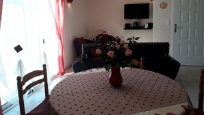 Uma área de refeições com uma mesa redonda coberta por uma toalha de bolinhas, um vaso com flores e um sofá preto ao fundo.