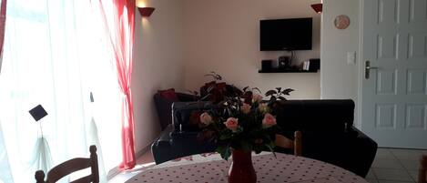 Un área de comedor con una mesa redonda cubierta por un mantel de lunares, un jarrón con flores y un sofá negro al fondo.