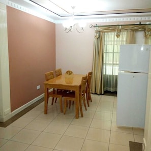 Cozy living space with a dining area, featuring a dining table and six chairs, a refrigerator, and a window with curtains.