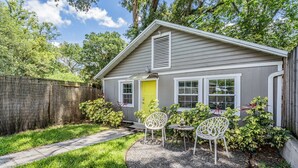 Une petite maison avec un porche à l’avant, une porte jaune et une fenêtre avec des volets.