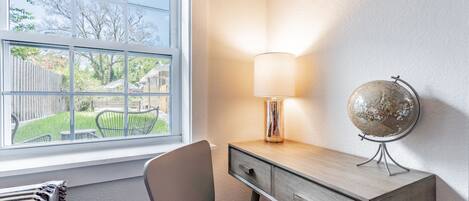 A study room with a desk, chair, lamp, globe, and a window with a view of a garden.