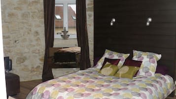 A bedroom with a stone wall, a wooden bed, a nightstand, and a window with curtains.
