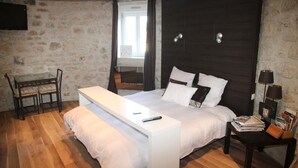 A bedroom with a stone wall, a bed with white bedding, a bedside table with a lamp, and a TV mounted on the wall. - atypical cottage with heated pool and covered in a beautiful & calm (Bruyères-et-Montbérault)