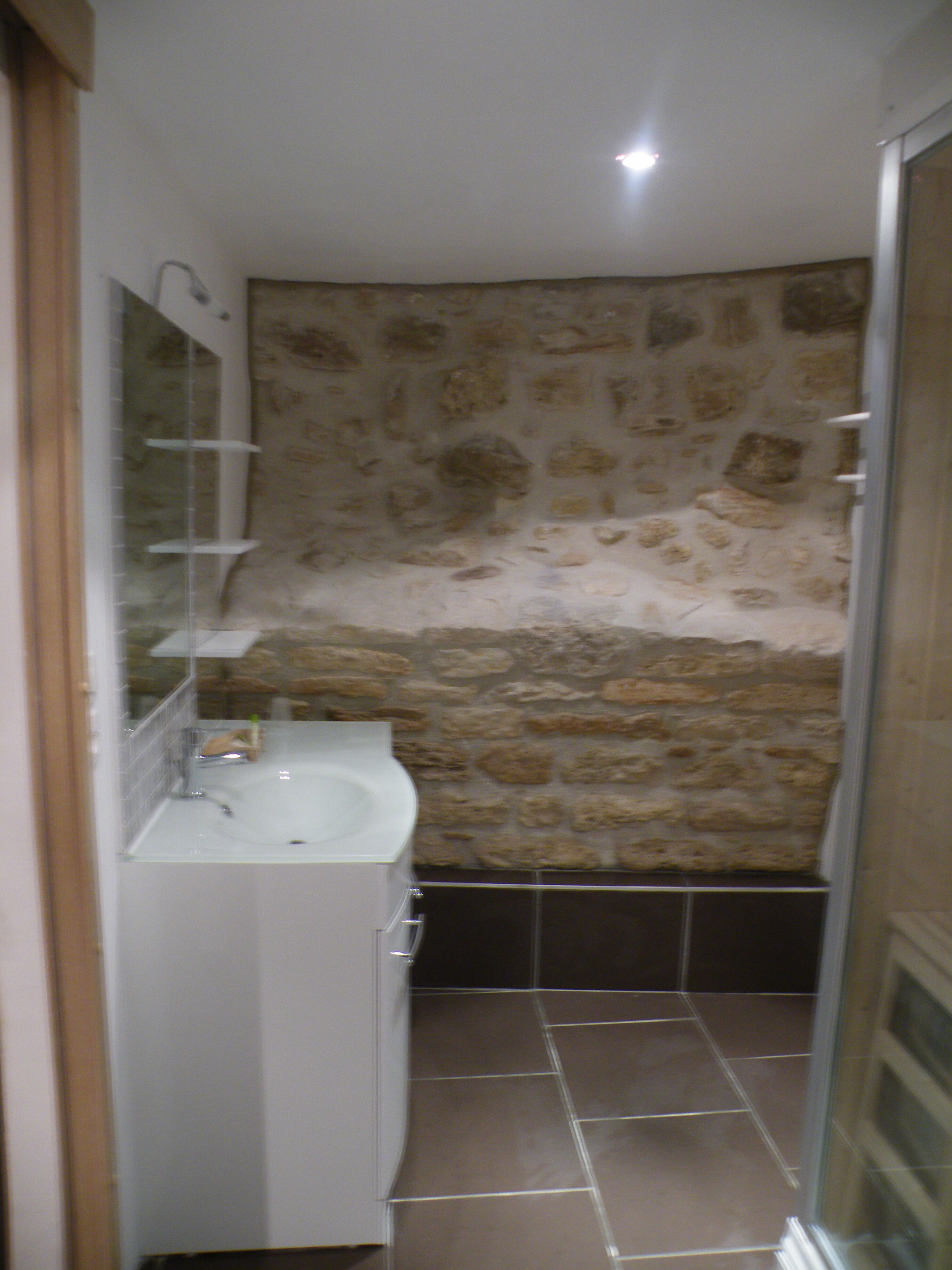A bathroom with a stone wall, a white sink, and a mirror.