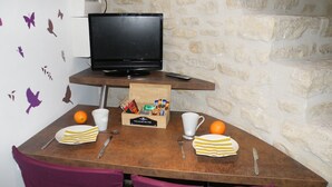 A dining table with a laptop, a remote control, and a box of chocolates. There are two chairs, a cup, a plate, and a fork on the table. - atypical cottage with heated pool and covered in a beautiful & calm (Bruyères-et-Montbérault)