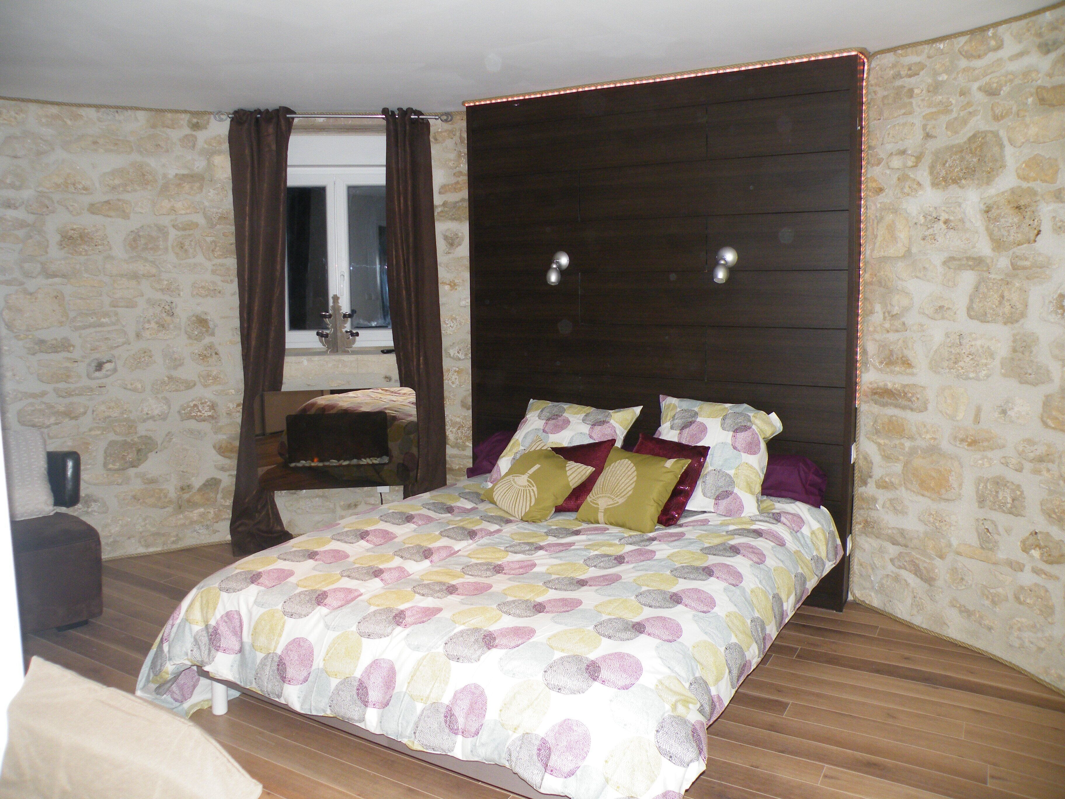 Une chambre avec un mur en pierre, une tête de lit en bois et un lit recouvert d’une couvre-lit à motifs.
