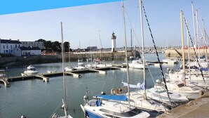 Uma marina com barcos atracados, um farol e edifícios ao fundo.
