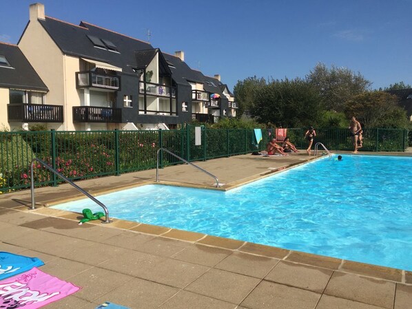 Une piscine entourée d’une clôture verte, un poste de surveillance pour les sauveteurs et une personne dans l’eau.