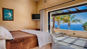 Une chambre d’hôtel avec un lit, une télévision, un tableau et un balcon offrant une vue sur l’océan et les palmiers.