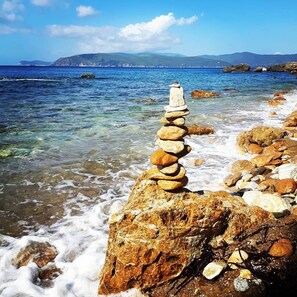 A coastal scene with a stack of stones on a rock, clear water, and distant mountains. - CHARMING VILLINO DEI PEDUCELLI DIRECTLY ON THE SEA! (Capoliveri)