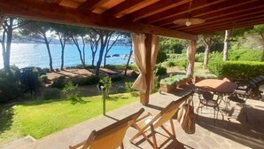 Un espace extérieur aménagé, abrité et doté de sièges, offrant une vue sur la mer, une pelouse et un jardin.