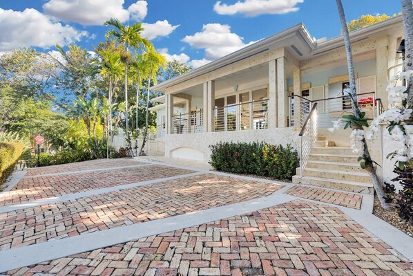 A building with a covered porch, a brick driveway, and a staircase leading to the entrance.