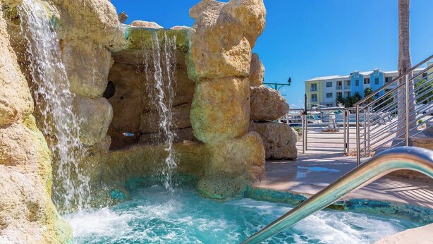 Una formazione rocciosa con una cascata, una piscina e una scalinata che conduce a un edificio.