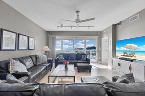 Una sala moderna con un sofá de cuero, una mesa de centro y un televisor mostrando una escena de playa.