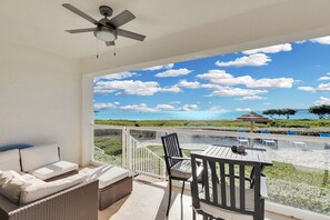A balcony with a view of the sea, a ceiling fan, and outdoor furniture.