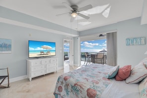 A bedroom with a bed, a television, a ceiling fan, a dresser, and a view of the ocean.