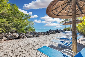 A beach with lounge chairs and a thatched umbrella. - Mariners Club # 314  3 Bed 2.5 Bath Key Largo Beachfront Luxury Ocean views and 3 bedroom 2.5 bath condo (Key Largo)