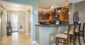 A modern kitchen with a central island, bar stools, and a clock on the wall.