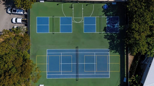 Vista aérea de un complejo de canchas de tenis con múltiples canchas, rodeado de árboles y un área de estacionamiento.