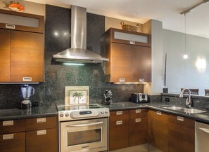 Une cuisine moderne avec des meubles en bois, une hotte en acier inoxydable, un four encastré, un grille-pain et un plan de travail en granit.