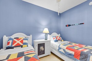 A bedroom with two beds, a nightstand, a lamp, and a wall-mounted object.