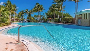Piscina cristallina con indicatore di profondità di 2,7 metri, circondata da palme e lettini da relax.