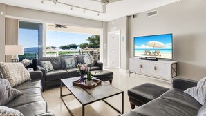 Un ampio soggiorno con una grande TV, divani in pelle, un tavolino da caffè e vista sulla spiaggia.