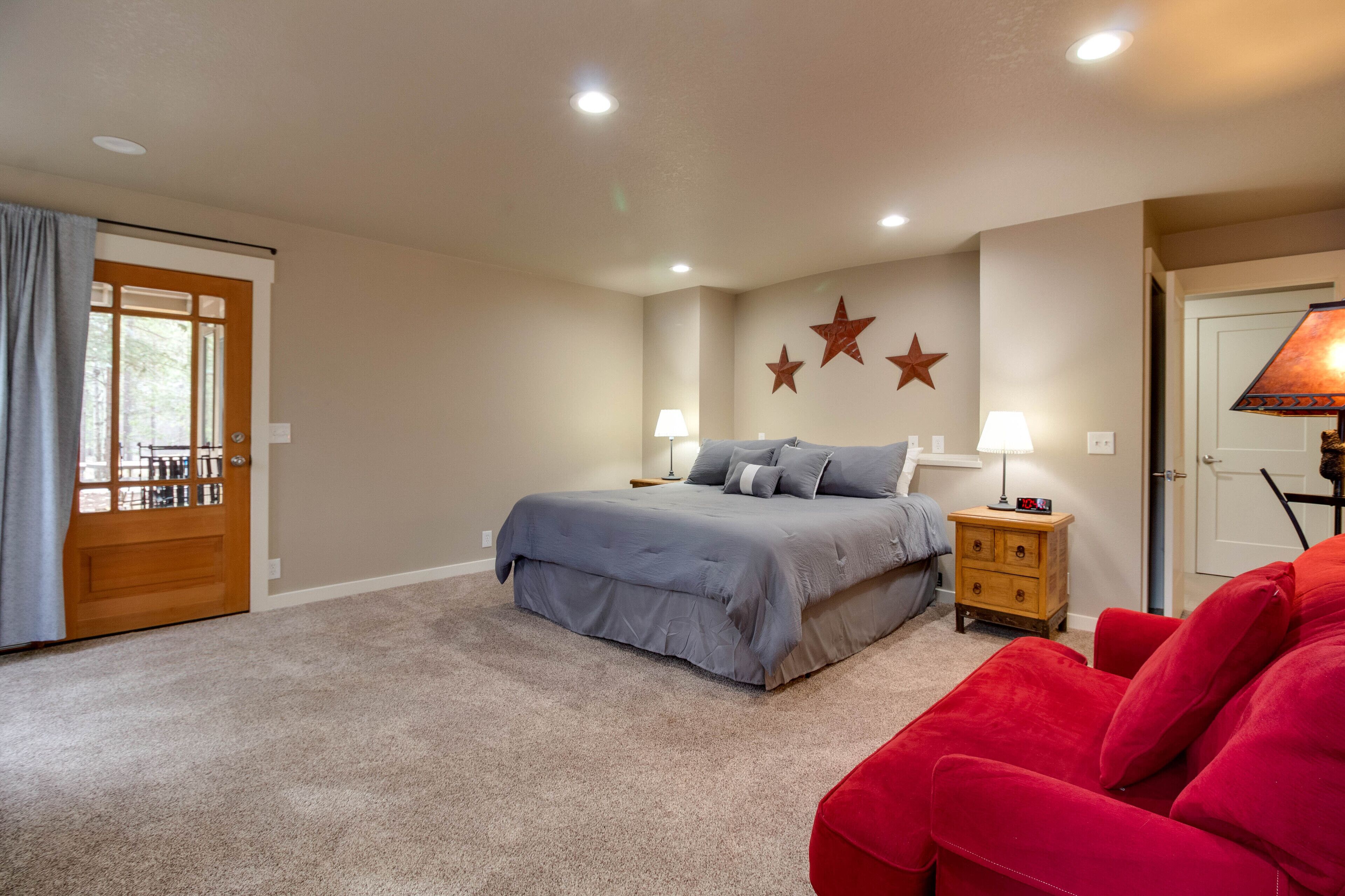 A bedroom with a bed, nightstands, a red chair, and a door with a view.