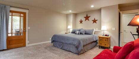 A bedroom with a bed, nightstands, a red chair, and a door with a view.