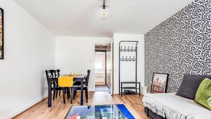A modern living room with a dining area, a glass coffee table, a patterned wall, and a sofa with a throw blanket.