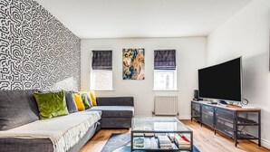 A modern living room with a grey sofa, a glass coffee table, and a flat-screen TV.