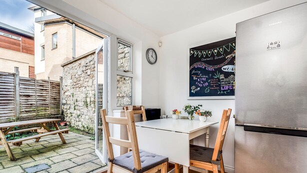 A compact kitchen with a stainless steel refrigerator, a white table, and two wooden chairs.