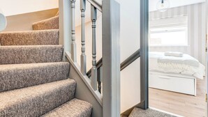 A staircase with a textured carpet and wooden balusters leading to a bedroom with a bed and a window.