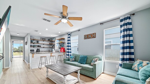 A modern living room with a sofa, a coffee table, and a kitchen area with a microwave and shelves. - DOG FRIENDLY! EAST SIDE OF DUPLEX, PRIVATE BALCONY - BEACHBALL PROPERTIES (Gulf Shores)