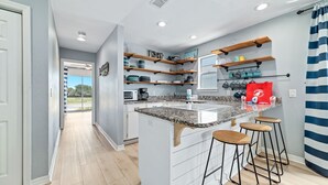 A modern kitchen with a central island, bar stools, and built-in shelves. - DOG FRIENDLY! EAST SIDE OF DUPLEX, PRIVATE BALCONY - BEACHBALL PROPERTIES (Gulf Shores)