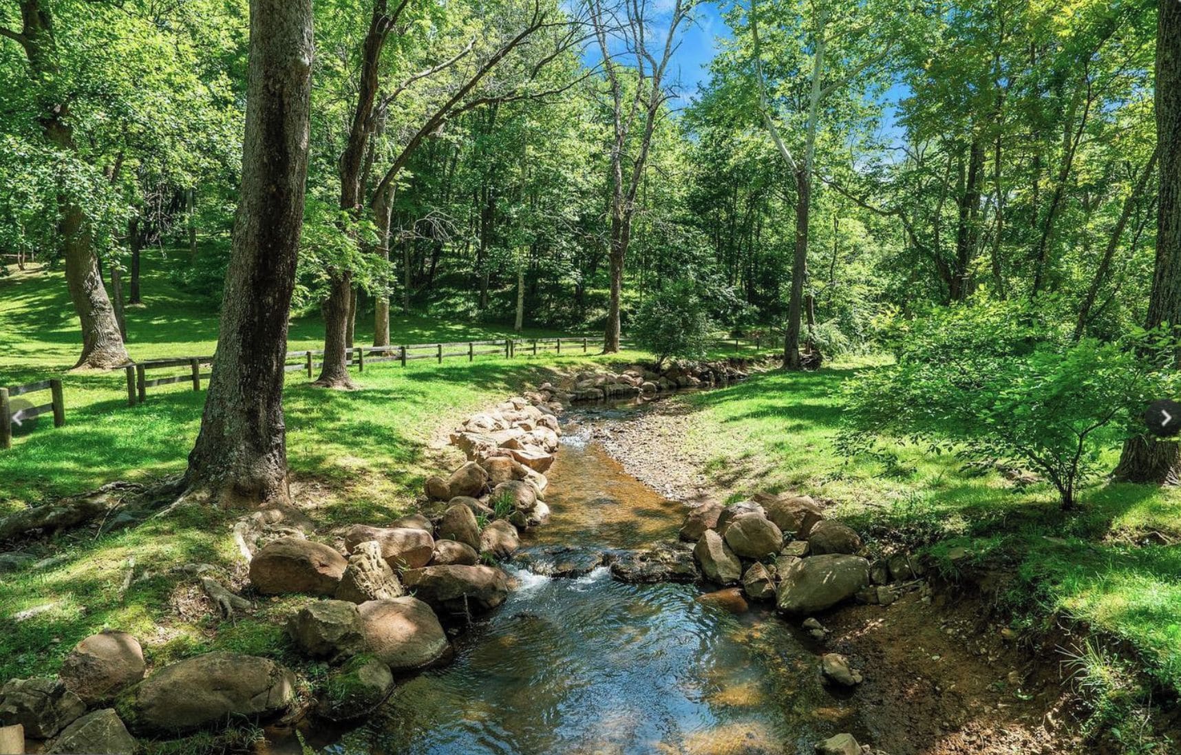 A serene forest stream with a wooden bridge and a wooden fence.