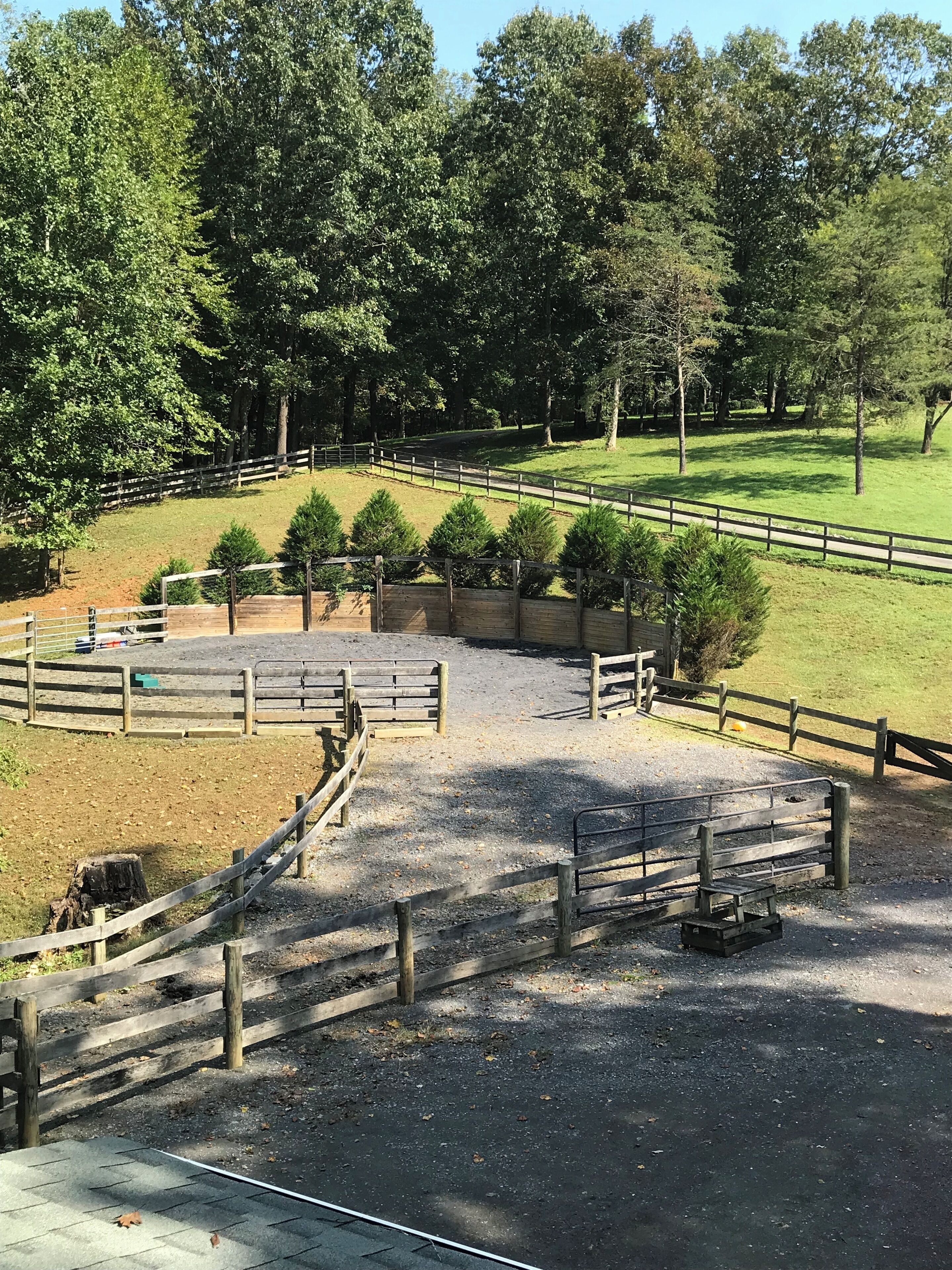 A fenced outdoor area with a gravel path, surrounded by trees and grassy fields.