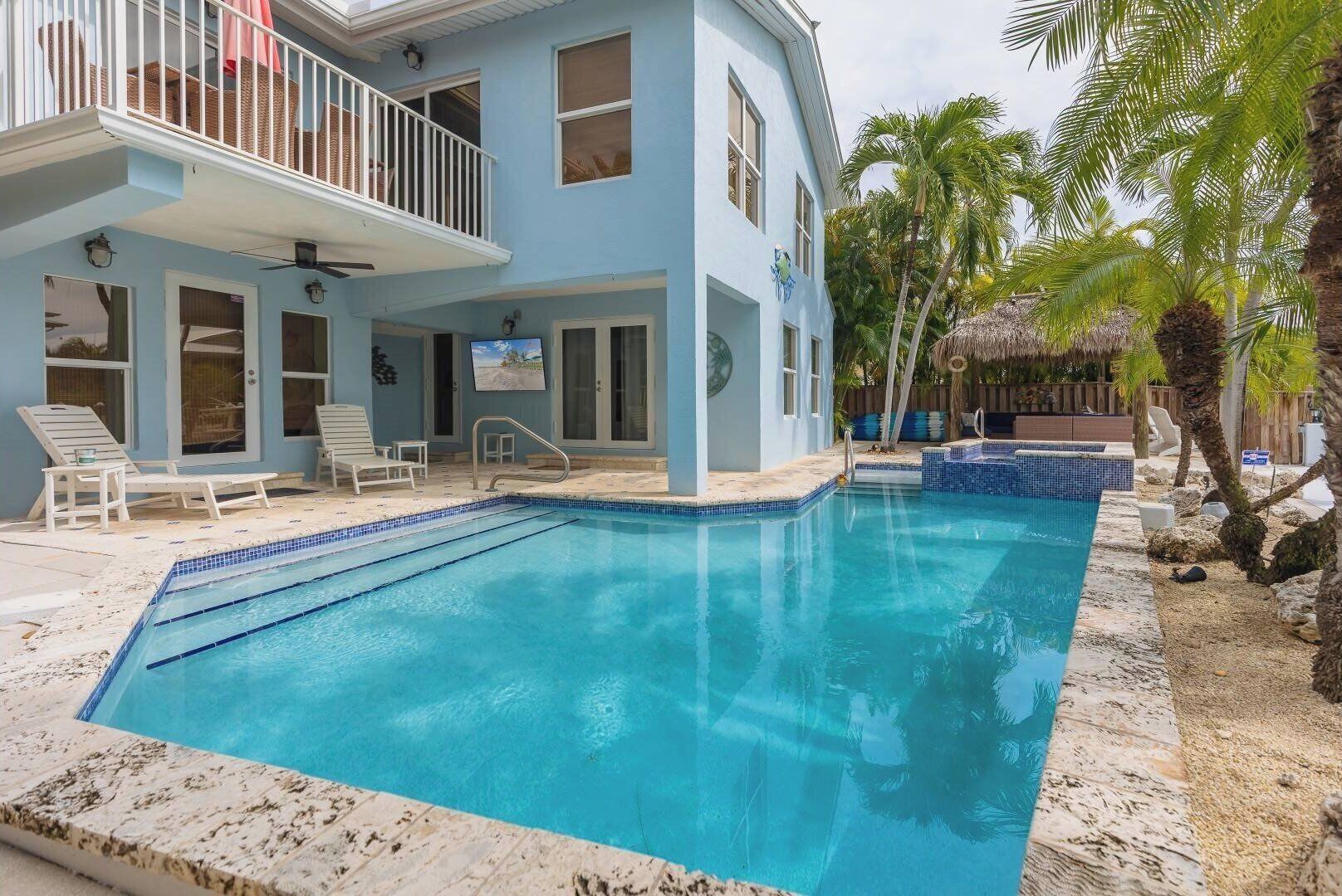 A two-story building with a swimming pool, lounge chairs, and palm trees.