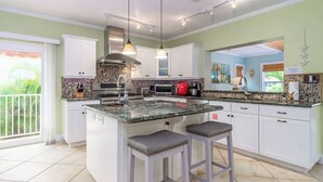 Una cocina moderna con una isla central, muebles blancos y un amplio ventanal.