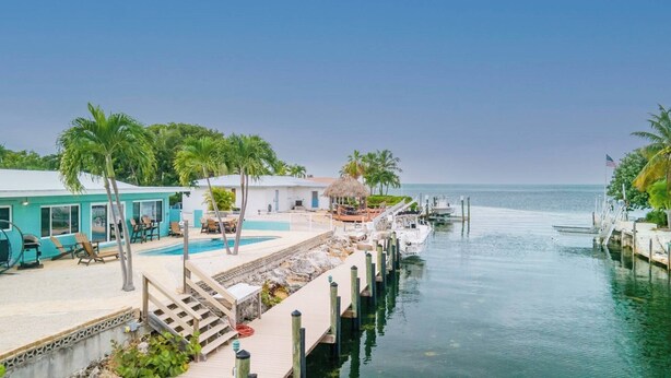 A waterfront property with a swimming pool, outdoor seating, and a dock. - Yellowtail for Dinner – Ground-Level Waterfront 3BR Home with Pool & Dock on the Gulfside (Marathon)