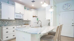 A kitchen with white cabinets, a marble countertop, a sink, and a wooden chair. - Yellowtail for Dinner – Ground-Level Waterfront 3BR Home with Pool & Dock on the Gulfside (Marathon)