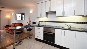 Een moderne keuken met witte kasten, een zwart aanrecht en roestvrijstalen apparatuur. Er is een zithoek met een bruine leren bank en twee barkrukken.