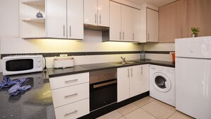 Een moderne keuken met witte kastjes, een magnetron, een broodrooster, een spoelbak en een wasmachine.