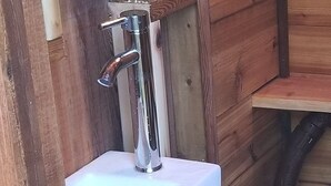 A rustic wooden bathroom with a white sink, a small shelf with decorative items, and a toilet. - Emerald Forest Treehouse - From Treehouse Masters (Redmond)