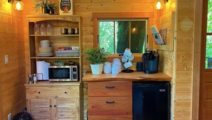 A compact kitchen with wooden walls, a microwave, a coffee maker, and a black refrigerator. - Emerald Forest Treehouse - From Treehouse Masters (Redmond)